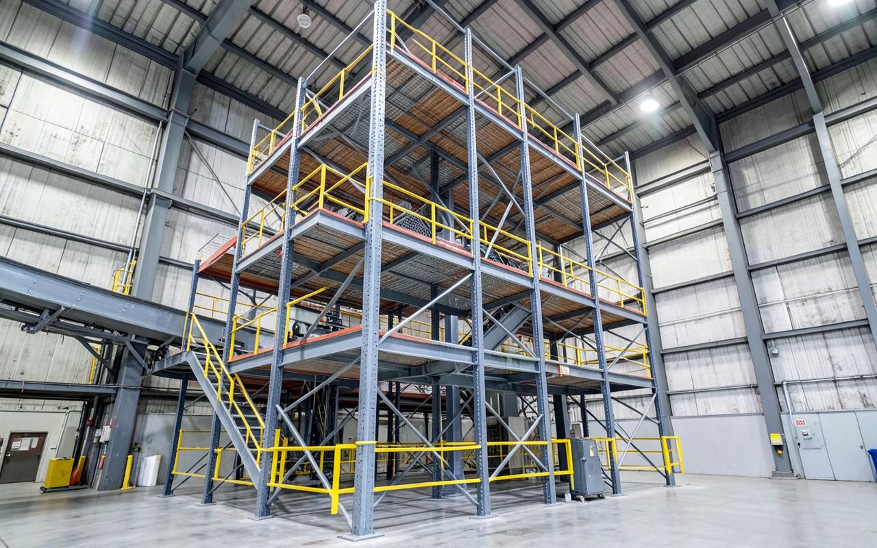 Three-tier steel pick tower with walkways and conveyor inside a high-bay warehouse